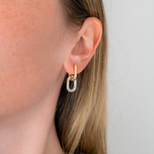 Close-up of an ear wearing a gold and silver hoop earring against a neutral background
